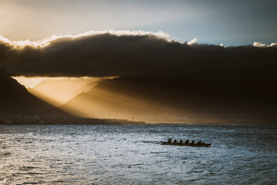 Silhouette of athletes in outrigger canoe, paddle wile the sun sets.