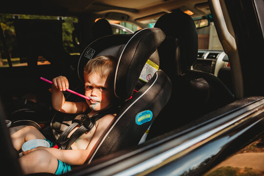 Young Boy With Grumpy Face Drinking From Straw In Car Seat