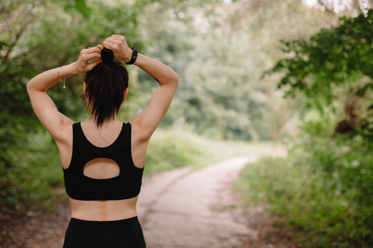 Rear view of female jogger making hair bun at park