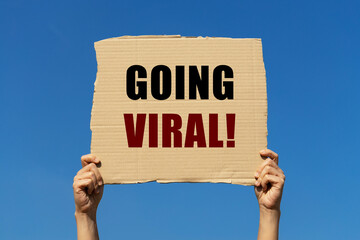 Going viral on box paper held by 2 hands with isolated blue sky background. This message board can...