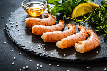 Prepared raw prawns with thyme, lemon, and coriander  on black stone plate
