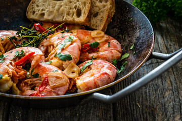 Fried prawns with thyme in cooking pan on wooden table
