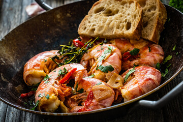 Fried prawns with thyme in cooking pan on wooden table
