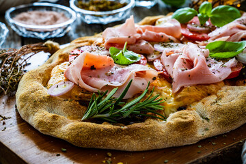 Pinsa Romana with cooked ham, mozzarella and vegetables on wooden table