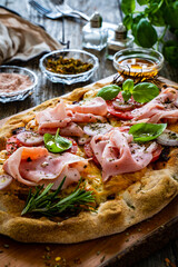 Pinsa Romana with cooked ham, mozzarella and vegetables on wooden table