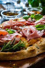 Pinsa Romana with cooked ham, mozzarella and vegetables on wooden table
