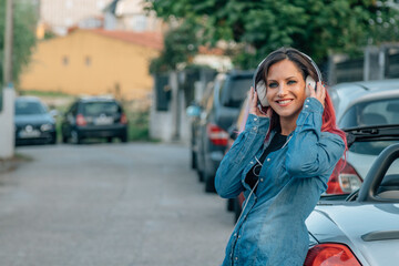 Fototapeta na wymiar smiling girl with headphones on the street next to the car
