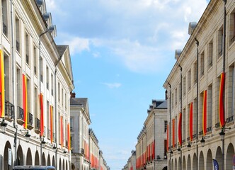 Cobbled street lined with old houses decorated with banners in medieval colors: red and yellow on the occasion of the Jeanne d'Arc festival, perspective view.