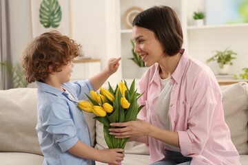 Fototapeta na wymiar Happy woman with her cute son and bouquet of beautiful flowers at home. Mother's day celebration