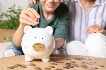 Obraz na płótnie Canvas Boy with his mother putting coin into piggy bank at home, closeup