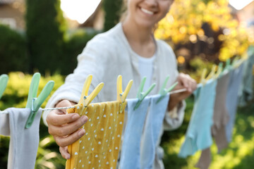 Closeup view of smiling woman hanging baby clothes with clothespins on washing line for drying in backyard