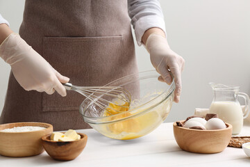 Woman whisking crepe batter in glass bowl at white wooden table, closeup