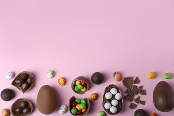 Tasty chocolate eggs and candies on pink background, flat lay. Space for text