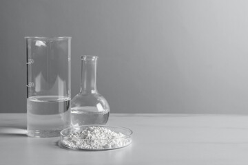 Petri dish with calcium carbonate powder and laboratory glassware on white table. Space for text - obrazy, fototapety, plakaty