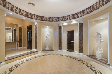 Round lobby wellness spa center, decorated in Greek style with painted walls and statues in niches.