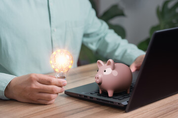 Man holding a light bulb while working on a computer to think and generate new ideas for business...