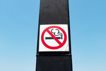 High angle photo no smoking signs old circle red white attached to a black steel pole. Blue sky...