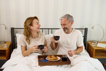 Mature couple enjoying coffee and breakfast in bed