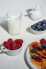 Overhead view of plate with pancakes, blueberries, raspberries and glass of milk, on white table, selective focus, vertical