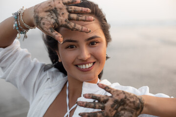 Beautiful young asian woman in white shirt smiles fervently and cheerfully, showing open palms in patterns of wet sand. 