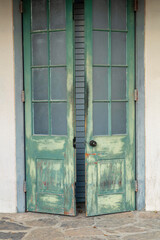 Green wooden door exterior with white building facade with aged and weathered facade and black door handle