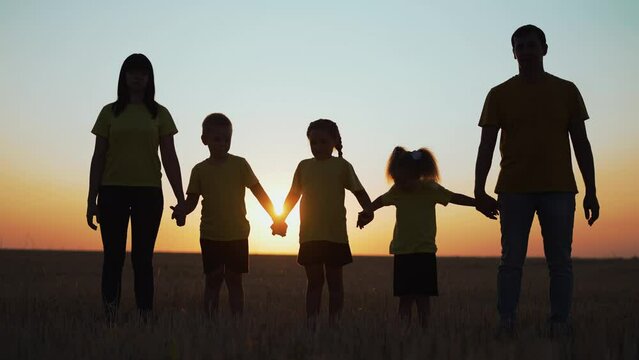 Silhouette of a happy family. A group of people walk together holding hands. Parents and children have fun walking at sunset in the natural park. Active people outdoors in park. boy and girl together