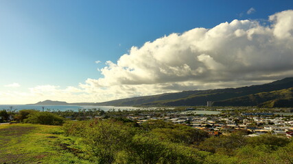 Fototapeta premium Scenic panoramic view over Hawaii Kai suburbs and surrounding mountain landscape as clouds build on a sunny day, with Diamond Head in the distance. Near Honolulu, Hawaii.