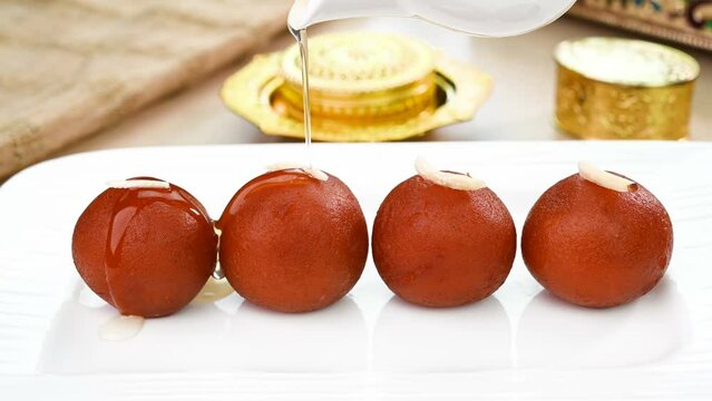 Pouring sugar syrup on gulab jamun sweet, served in a plate.