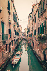 Old narrow canal in Venice with green water, medieval houses on the sides and boats (vintage photo effect)