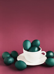 green color Easter eggs in white cup on wine red background