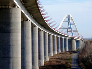 white basket handle arch design steel suspension bridge. heavy support cables. modern leaning red street light. transportation concept. blue sky. diminishing perspective. Pentele bridge in Hungary