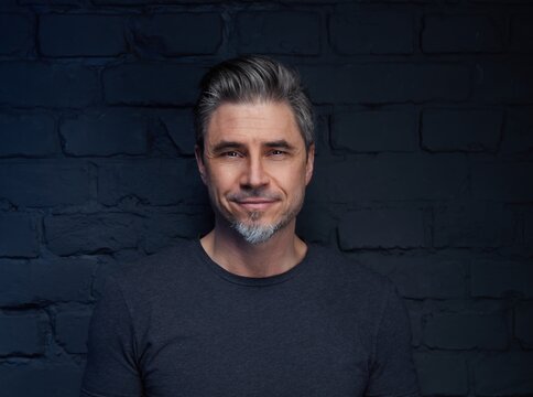 Middle Aged Good Looking Casual In Front Of Black Brick Wall, Smiling. Portrait Of Mid Adult, Mature Age Man,