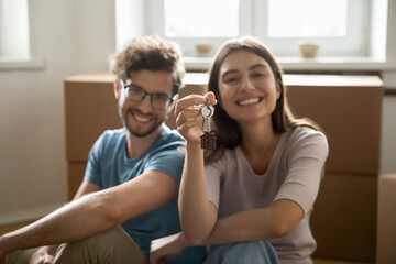 Happy young couple showing keys from hew home together, looking at camera, smiling, sitting at...