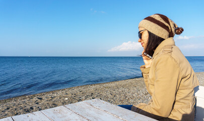 Young woman talking on the phone at beach. Blank copy space on blue sky.