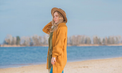 Woman in wool yellow cardigan, fedora hat and blue jeans at the beach, new collection, fashionable trend