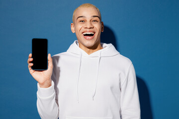 Young happy dyed blond man of African American ethnicity wear white hoody hold use mobile cell phone with blank screen workspace area isolated on plain dark royal navy blue background studio portrait.