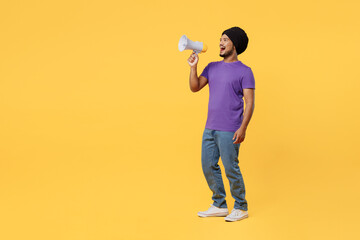 Full body devotee Sikh Indian man ties his traditional turban dastar wears purple t-shirt hold megaphone scream announces discounts sale Hurry up isolated on plain yellow background studio portrait.