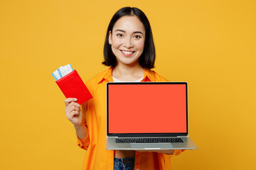 Young woman wear casual clothes use holding work passport ticket laptop pc computer isolated on plain yellow background. Tourist travel abroad in free time rest getaway Air flight trip journey concept