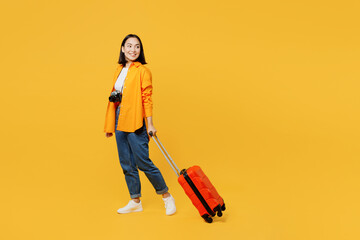 Young woman wear summer casual clothes walk go with suitcase bag look aside isolated on plain yellow background. Tourist travel abroad in free spare time rest getaway. Air flight trip journey concept. - obrazy, fototapety, plakaty