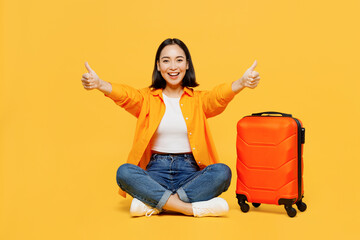 Young woman wear summer casual clothes sit suitcase show thubmb up gesture isolated on plain yellow background. Tourist travel abroad in free spare time rest getaway. Air flight trip journey concept. - obrazy, fototapety, plakaty