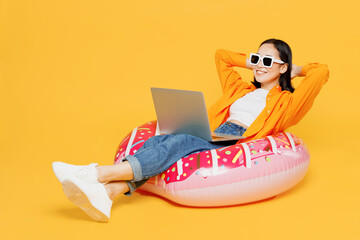 Young woman wear summer clothes sit on rubber ring use laptop pc computer isolated on plain yellow background. Tourist travel abroad in free spare time rest getaway. Air flight trip journey concept.