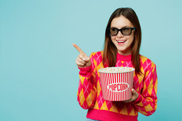 Young fun cheerful smiling happy woman in 3d glasses wear casual clothes watch movie film hold bucket of popcorn cup of soda pop in cinema isolated on plain pastel light blue cyan background studio.