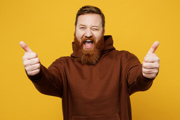 Young smiling cheerful fun redhead caucasian man wearing brown hoody casual clothes showing thumb...