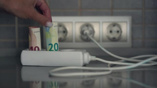 Female hand inserts twisted euro banknotes into electrical extension socket. Rise in electricity prices concept.