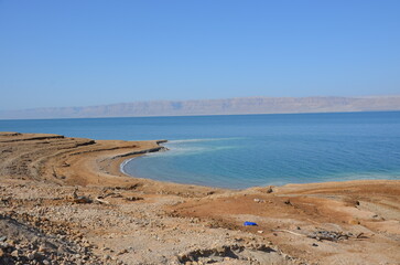 Panoramic view of the beautiful, clear blue Dead Sea shimmering and shining on a bright sunny day in Jordan and the dry land around it.