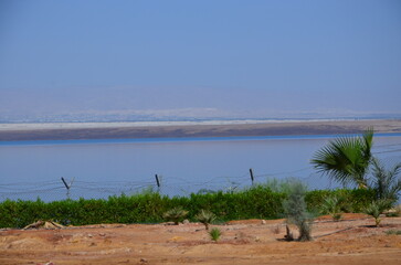 Panoramic view of the beautiful, clear blue Dead Sea shimmering and shining on a bright sunny day in Jordan and the dry land around it.