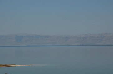 Panoramic view of the beautiful, clear blue Dead Sea shimmering and shining on a bright sunny day in Jordan and the dry land around it.