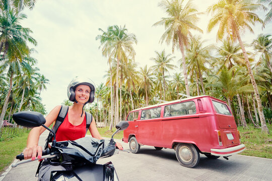 Tropical travel and transport. Young beautiful woman in helmet riding scooter on the road with palm trees.