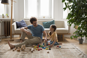Cheerful daddy and positive daughter kid enjoying leisure together, playtime at home, building toy...