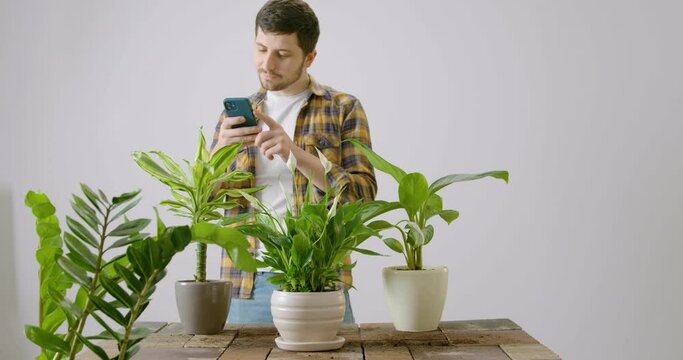 Bearded and cheerful man poses for indoor flowers after he replanted them, put fertilizers and sprinkled them with water. Male florist who loves flowers and has a hobby for taking care of green plants